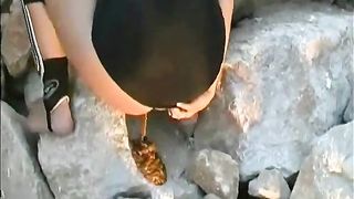Brunette hottie shitting diarheea on a big rock